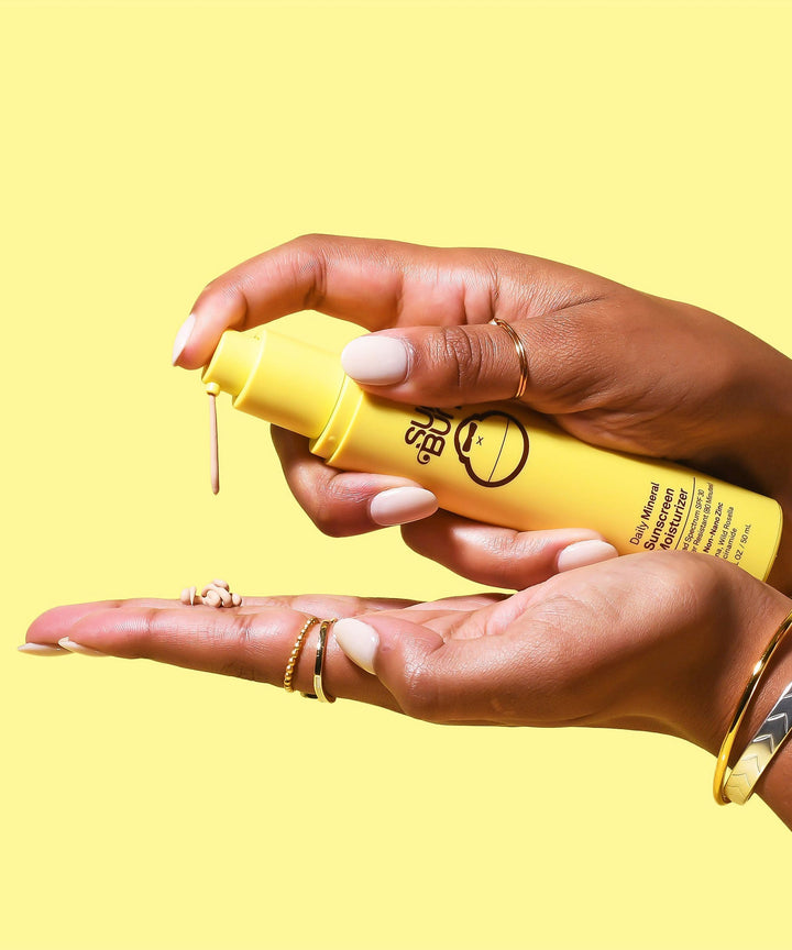 Hands dispensing Sun Bum Daily Mineral Sunscreen Moisturizer SPF 30 onto the palm, showcasing the product's creamy texture against a vibrant yellow background. Sun Bum.