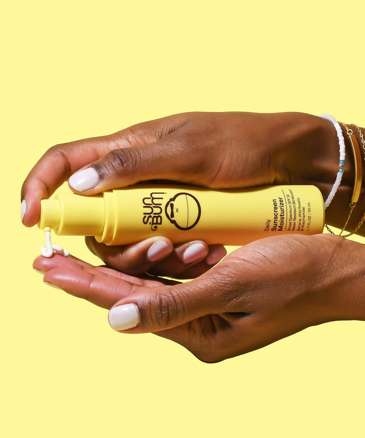 Hands holding a yellow bottle of Daily Sunscreen Moisturizer SPF 30 by Sun Bum, ready to dispense the product.