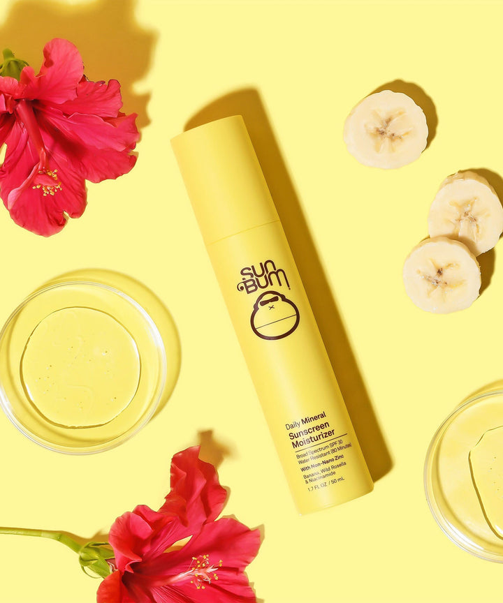 Lightweight Daily Mineral Sunscreen Moisturizer SPF 30 with antioxidant-rich Banana, Wild Rosella, and Niacinamide, surrounded by sliced bananas and red flowers. Sun Bum