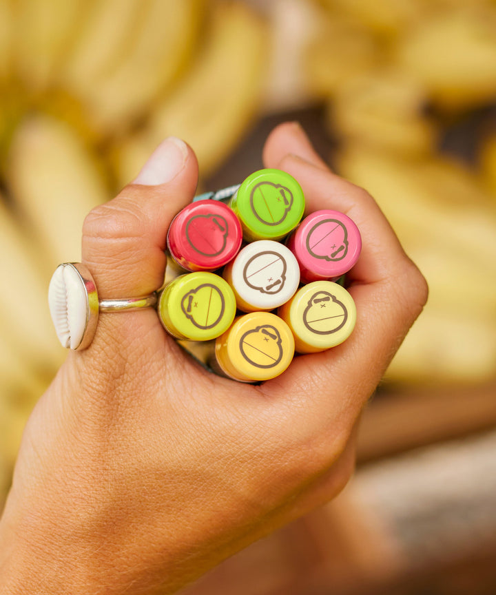 A hand holding a bunch of colorful Sun Bum SPF 30 Sunscreen Lip Balm tubes including Kiwi flavor, ideal for moisturizing and protecting with Aloe and Vitamin E. Sun Bum,
