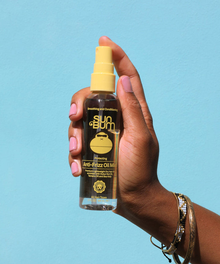 Hand holding a bottle of Anti-Frizz Oil Mist with Kukui Nut Oil and Tamanu Oil to combat humidity and frizz, from Sun Bum.