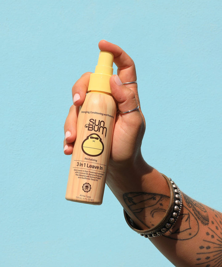Hand holding a bottle of Sun Bum 3 In 1 Leave In, a hair care product designed to detangle, condition, and protect hair. Sun Bum.