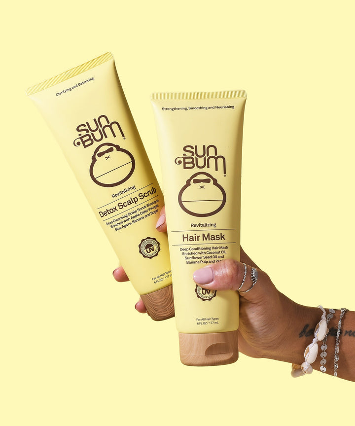 Two hands holding Sun Bum Detox Scalp Scrub and Revitalizing Hair Mask against a yellow background, designed to nourish and revitalize dry, damaged hair. Sun Bum.